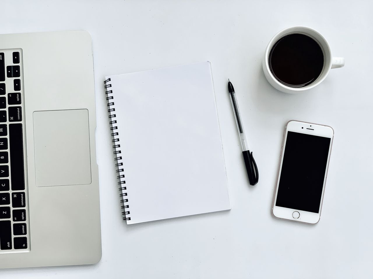 A tidy desk with a laptop, notebook and cup of coffee in soft daylight